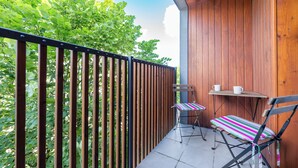Ein Balkon mit Holzlattenzaun, einem Tisch und zwei Stühlen sowie Blick auf Grünflächen.