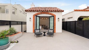Eine Terrasse mit zwei Stühlen und einem Tisch, eine gedeckte Terrasse und Blick in einen Raum mit einem Bett und einem Sessel.