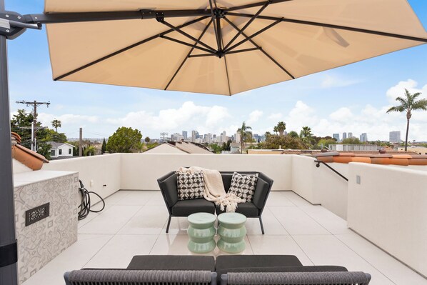 A rooftop terrace with a black sofa, two green stools, and a large beige umbrella. - Pristine and Central 4-bedroom home perfect for elegant entertaining/relaxation (Coronado)