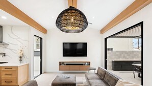 Ein modernes Wohnzimmer mit großem Fernseher, einer Couch und einem Essbereich, der durch eine offene Tür sichtbar ist.