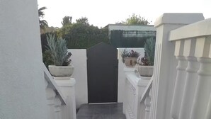 A narrow, tiled pathway leading to a gated entrance with white railings and potted plants.