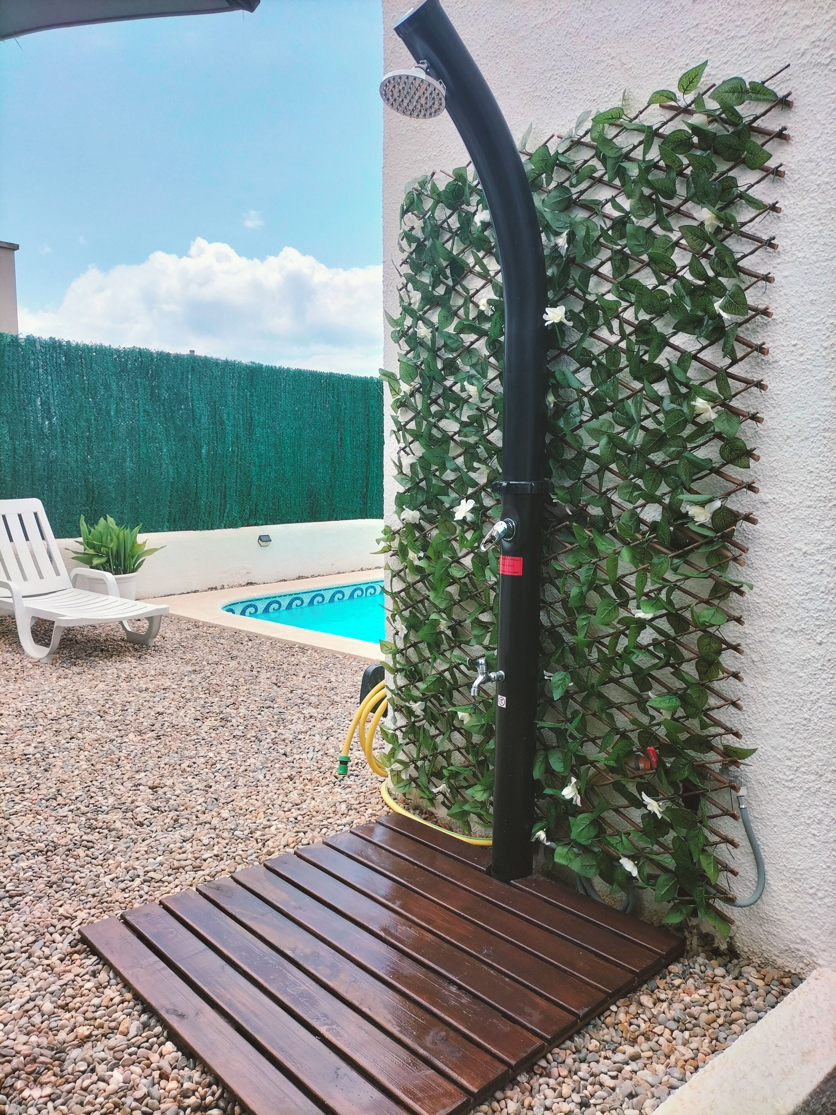 Ein Poolbereich mit Holzterrasse, einem weißen Stuhl und einer grünen Heckenwand.