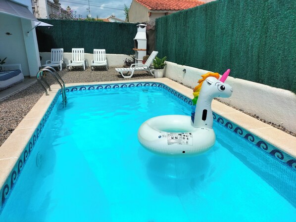 A swimming pool with a unicorn float, surrounded by white chairs and a green hedge. - House with private pool and ocean view (Cunit)