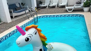 A swimming pool with a unicorn float, lounge chairs, and a covered seating area.