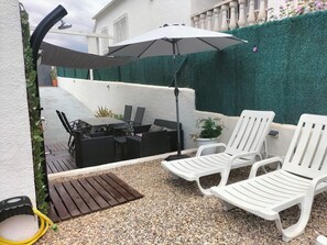 An outdoor patio with a table and chairs, a white umbrella, and a green hedge. - House with private pool and ocean view (Cunit)