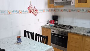Een keuken met een eettafel, stoelen, een fornuis, oven en kastjes.