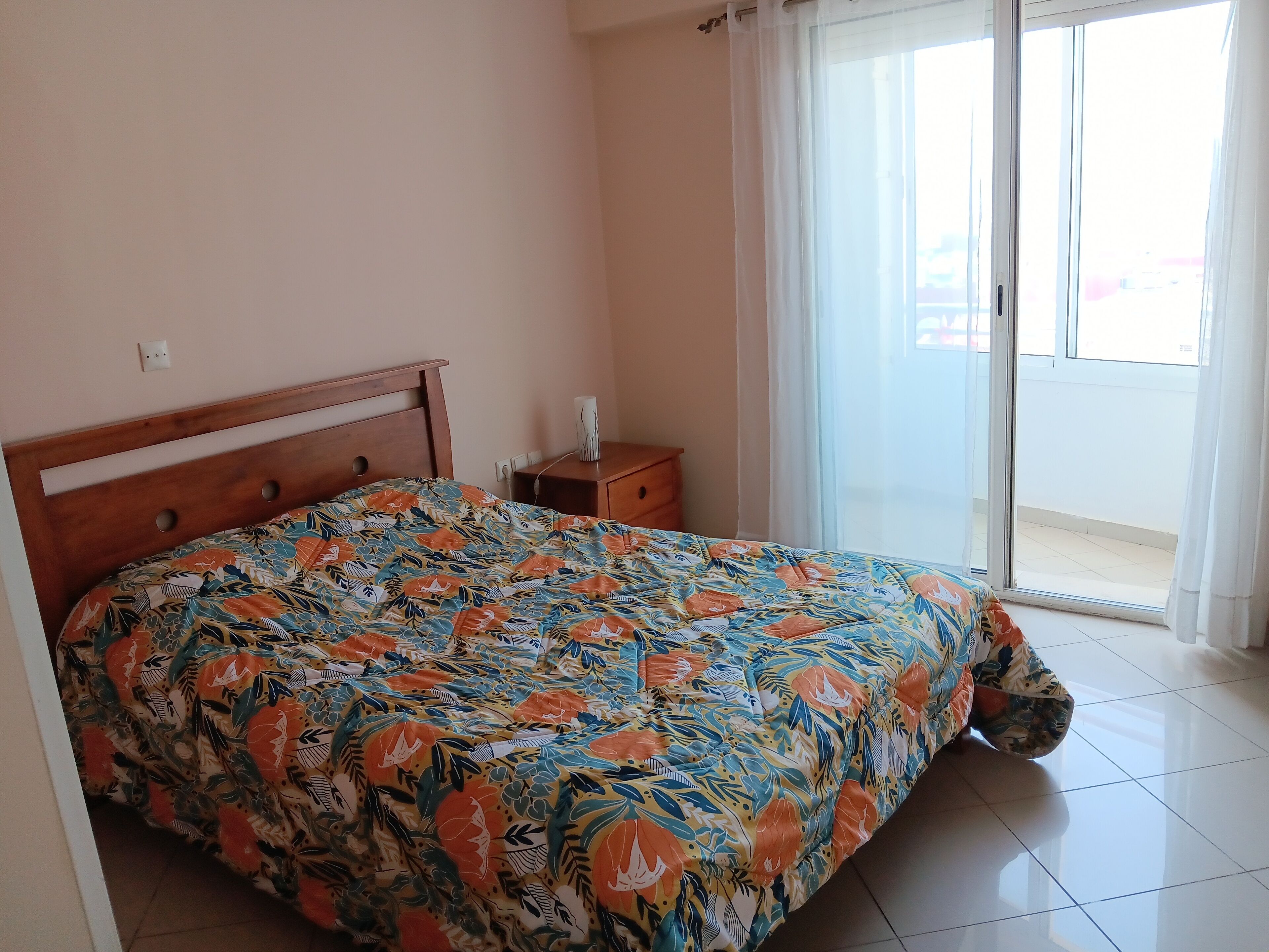Une chambre à coucher avec un lit, une table de chevet, une fenêtre avec des rideaux et une vue sur l’extérieur.