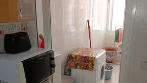 Een keuken met een magnetron, een wasmachine en een bezem die tegen de muur staat.