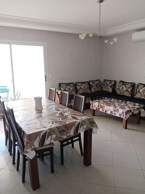 Un comedor con una larga mesa cubierta por un mantel estampado, rodeada de sillas de madera. Hay un banco con cojines estampados contra la pared.