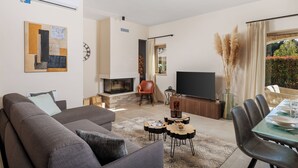 A modern living room with a sofa, a fireplace, a TV, and a dining area with a table set for four. - Sun  Spalato Villa Oblica (Jadruhi)