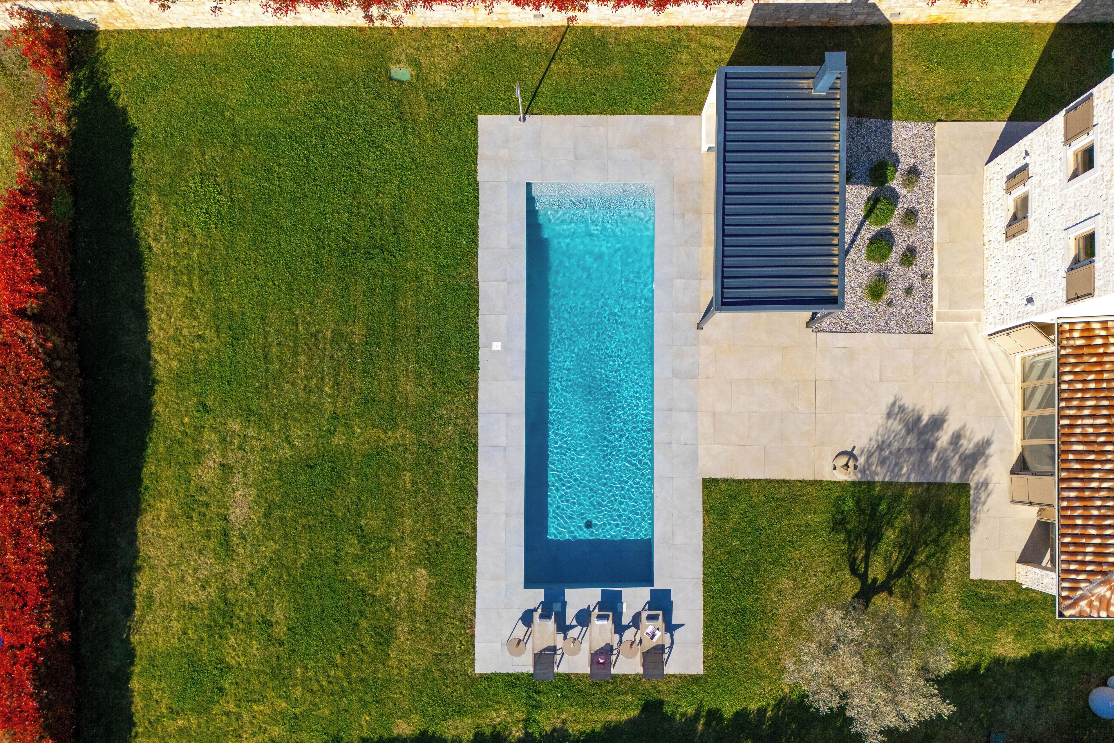 Vista aérea de una piscina con sillones de descanso, una terraza de piedra y un edificio con techo inclinado.