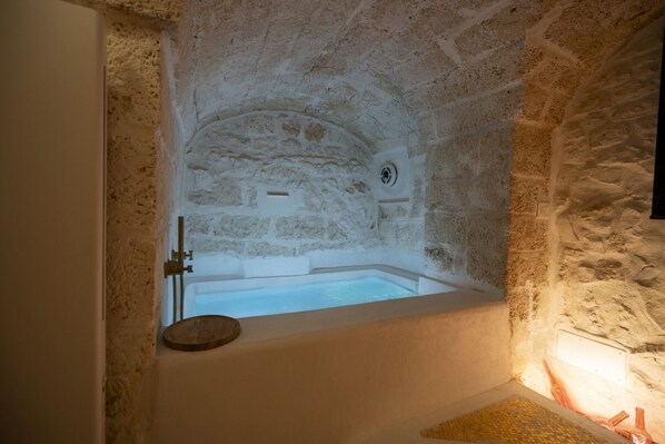 A stone-walled room with a bathtub, a wooden tray, and a circular window.