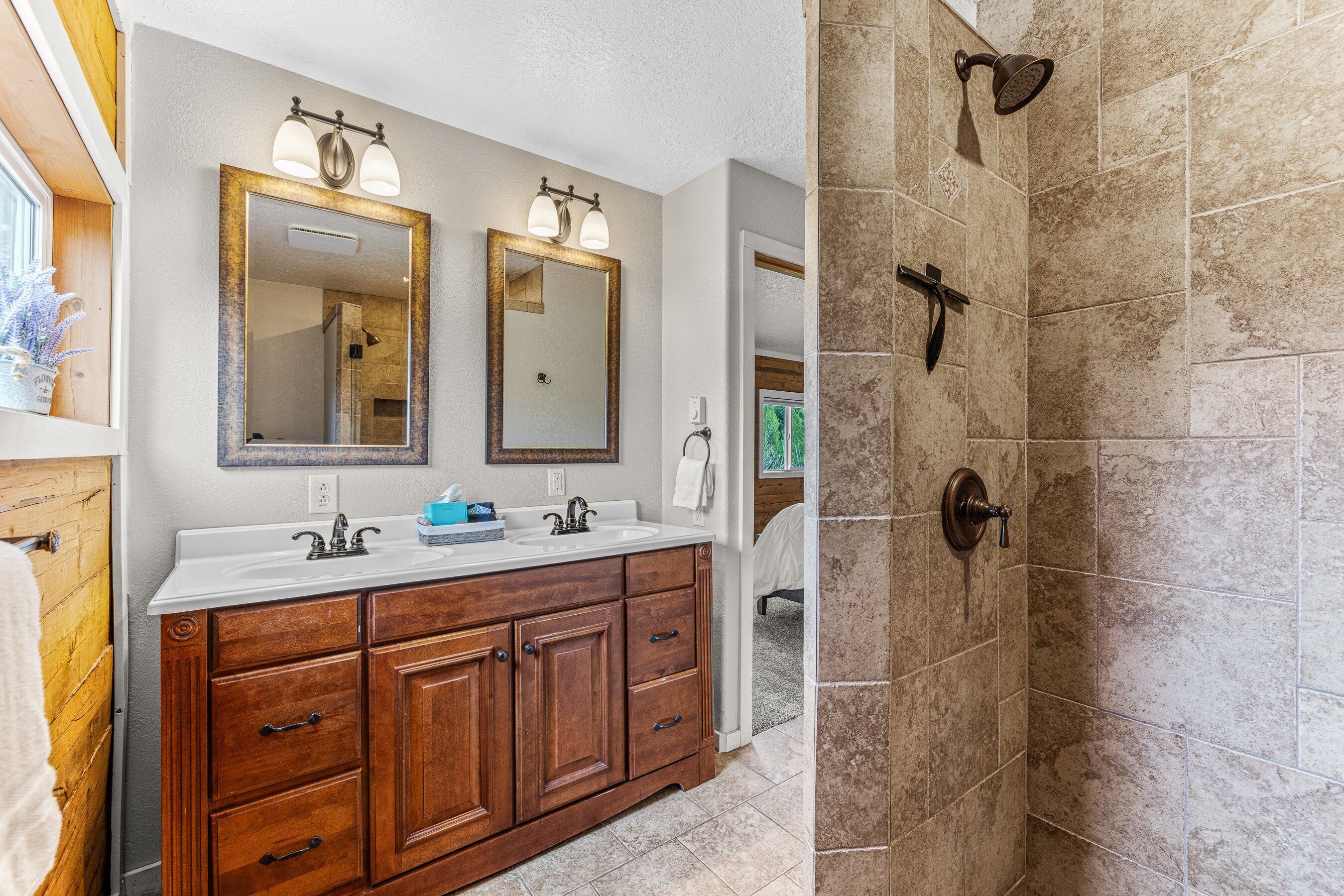 A bathroom with a double vanity, two mirrors, a shower with a wall-mounted showerhead, and a wooden cabinet.