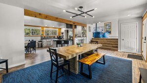 A spacious kitchen with a large wooden table and bench, a dining area with chairs, and a view of the outdoors through large windows. - Black Fork Lodge - Beautiful log home on 2.5 acres with trailer parking and panoramic views (McCall)