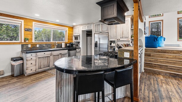 A spacious kitchen with a central island, wooden cabinets, and a large window. - Black Fork Lodge - Beautiful log home on 2.5 acres with trailer parking and panoramic views (McCall)
