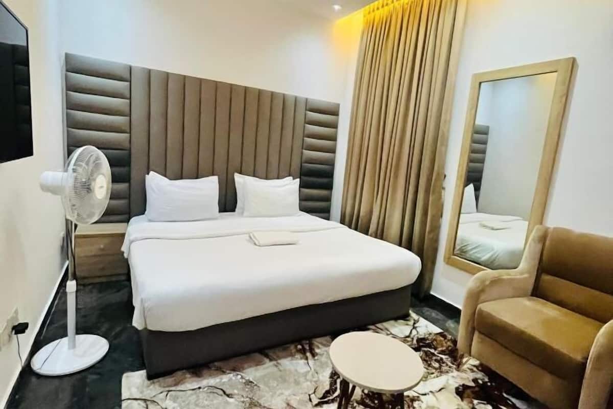 A modern hotel room with a large bed, a standing fan, a small round table, and a sofa.