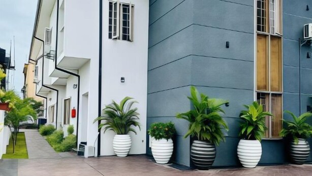 A modern building with a clean, geometric facade, large potted plants, and a paved walkway. - Diaggello Homes Apartment (Ibeju)