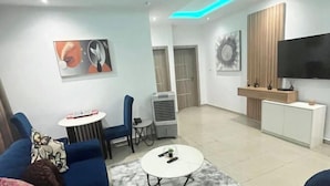 A modern living room with a blue sofa, a round coffee table, a flat-screen TV, and a small side table. - Diaggello Homes Apartment (Ibeju)