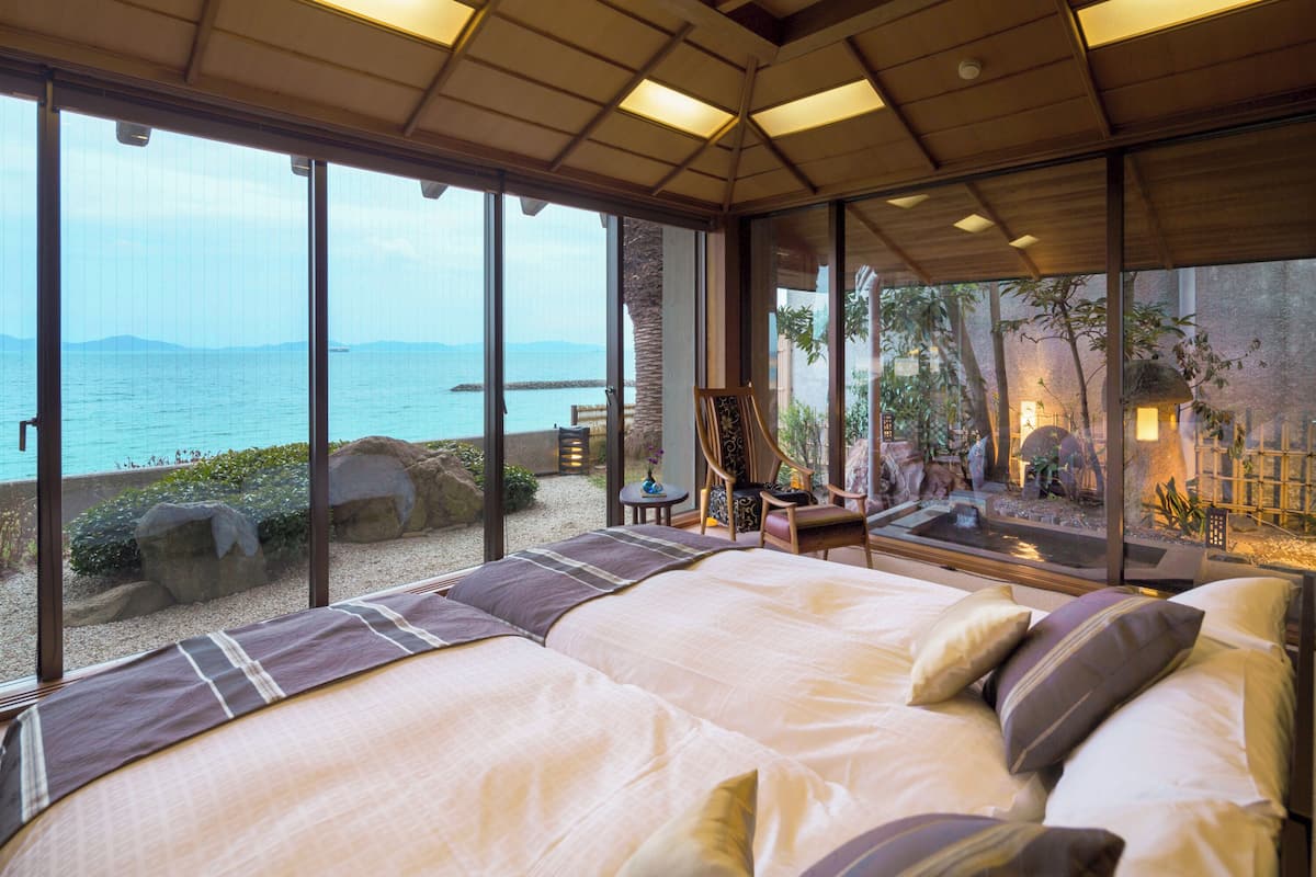 Ein Schlafzimmer mit einem großen Bett, Meerblick und einer kleinen Sitzecke mit Tisch und Stühlen.