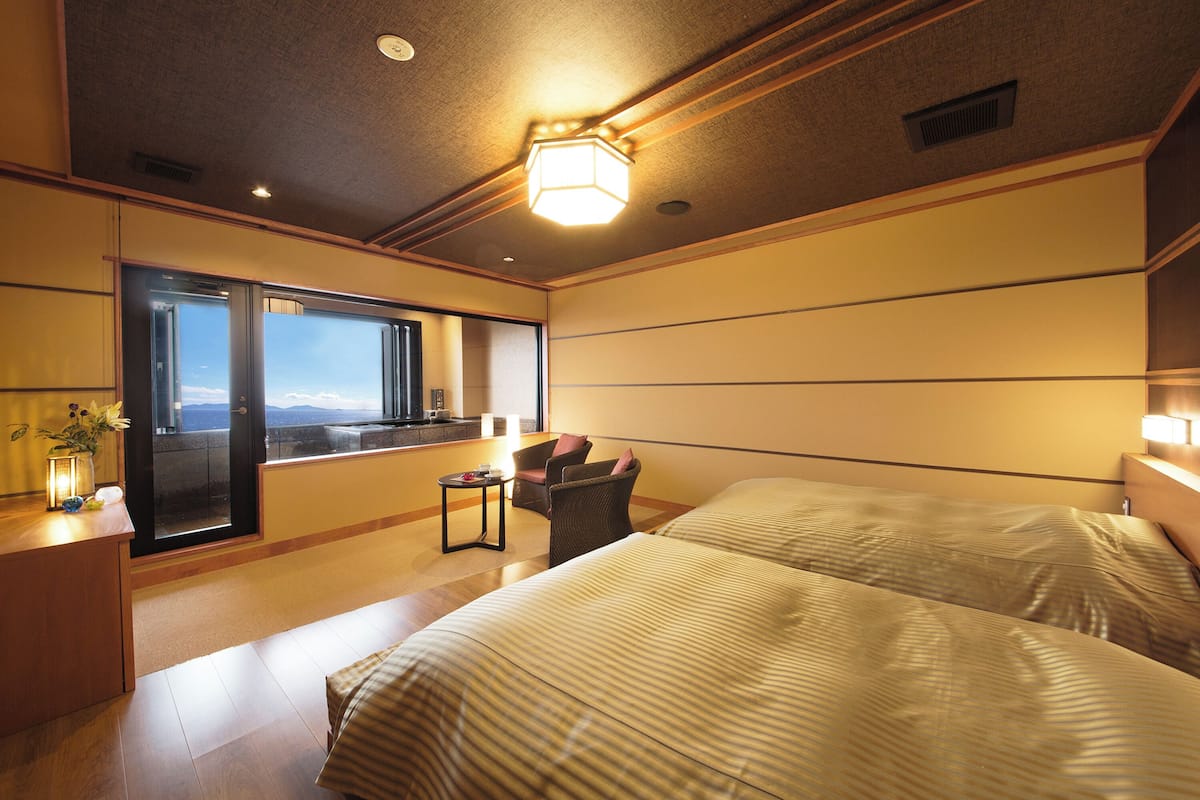 Ein Hotelzimmer mit zwei Betten, einem kleinen Tisch, einem Stuhl und einem großen Fenster mit Blick.