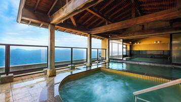 Un área de spa con hidromasaje y piscina, amplias ventanas con vistas al mar y una estructura de madera cubierta.