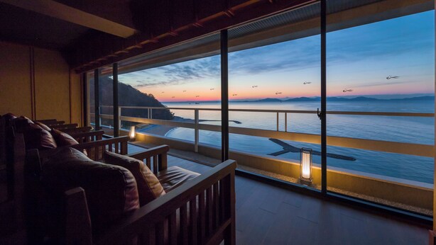 En balkon med havudsigt og solnedgang. Træstole og et bord med en lygte.