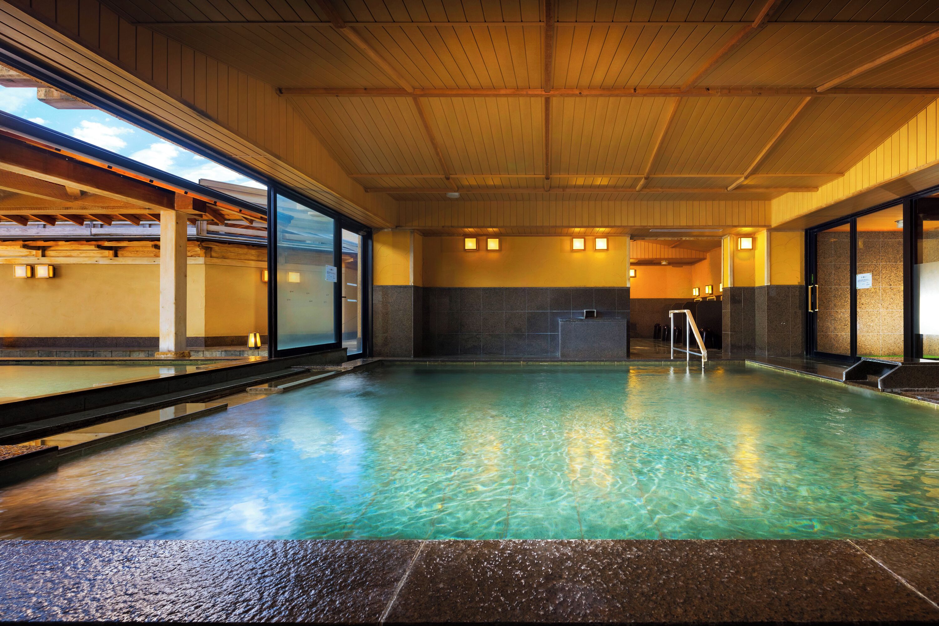 An indoor swimming pool with clear water, wooden ceiling beams, and tiled walls.