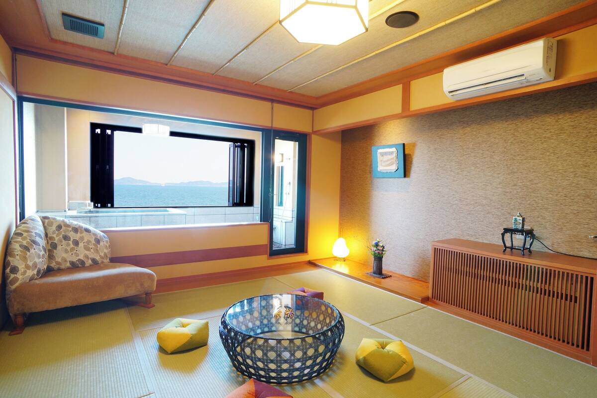 Ein traditioneller japanischer Raum mit Tatami-Böden, einem niedrigen Tisch, einer Couch und Blick auf das Meer.