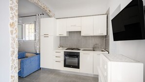 Une cuisine moderne avec des armoires blanches, un four encastré, un four à micro-ondes et un téléviseur noir fixé au mur.