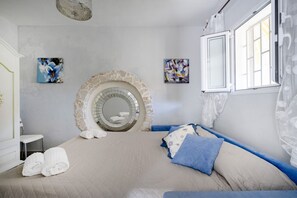 Un dormitorio con chimenea de piedra, cama con ropa de cama azul y beige, y obras de arte en las paredes.
