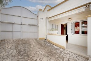 Un edificio blanco con un patio de piedra, una puerta de garaje blanca y una maceta pequeña blanca en el porche.