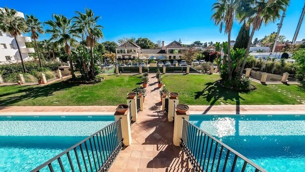 A pool area with a clear view of the pool, a pathway leading to the pool, and a building in the background.