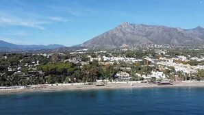 A coastal town with a mountain in the background, a beach, and buildings with greenery.