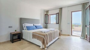 A bedroom with a bed, a nightstand, a window, and a view of the outdoors.