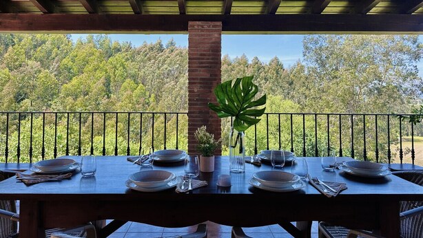 A dining table set for two with a view of a forested landscape.