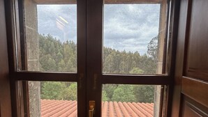 A window with a view of a red-tiled roof and trees.