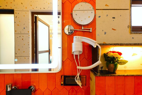 A bathroom with a mirror, a hairdryer, and a flower vase. - Chitralekha Boutique Resort (Dehradun)