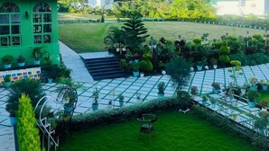 A green building with a thatched roof, a paved courtyard with potted plants, and a view of mountains in the background. - Chitralekha Boutique Resort (Dehradun)