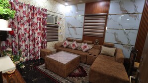 A living room with a brown sofa, a glass coffee table, a patterned rug, and a floral curtain. - Prem Aashiyana Home Stay (Agra)