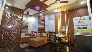 A modern living room with a sofa, a wooden chair, a table, and a decorative wall panel. - Prem Aashiyana Home Stay (Agra)