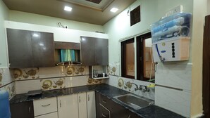 A kitchen with dark countertops, white cabinets, and a water dispenser. - Prem Aashiyana Home Stay (Agra)