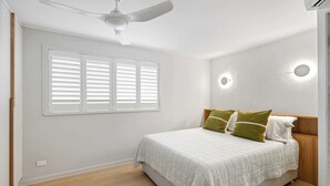 Un dormitorio con cama, ventilador de techo, ventana con persianas e iluminación empotrada en la pared.