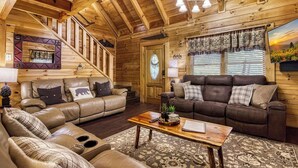 Ein gemütliches Blockhaus-Interieur mit zwei Ledersofas, einem Holztisch und einer Treppe, die zu einer oberen Ebene führt.