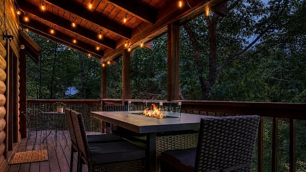 Eine Terrasse im Freien mit Tisch und Stühlen, einem Feuerbereich und einem Holgitter.