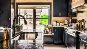 Une cuisine moderne avec des meubles de couleur sombre, un plan de travail en granit et une vue à travers une porte vitrée.