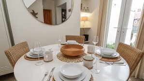 A round dining table with white plates, cutlery, and glassware, surrounded by wicker chairs.