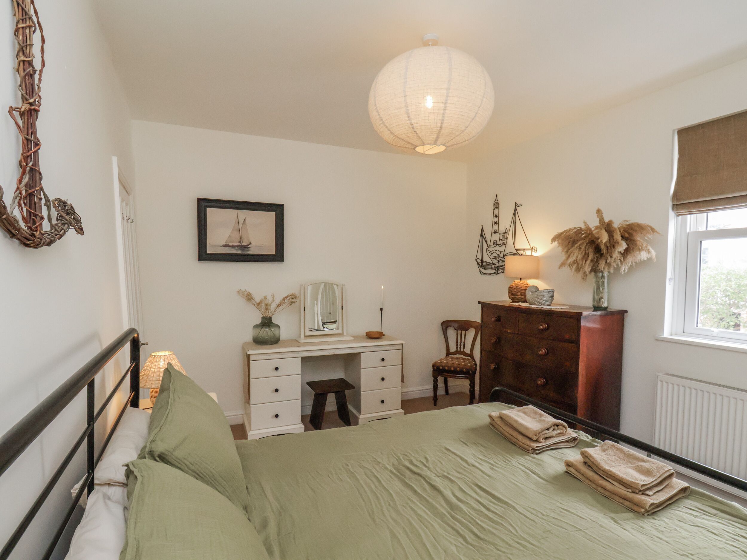 A bedroom with a bed, dresser, desk, chair, and a large window.