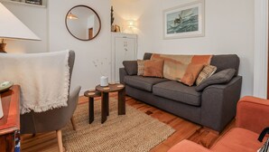 A living room with a grey sofa, a small round table, a mirror, and a lamp.