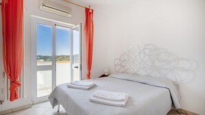 Ein Schlafzimmer mit Bett, weißen Vorhängen, Blick durch eine Glastür und einem weißen Kopfteil.
