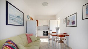 Ein Wohnzimmer mit einer Couch, einem Esstisch mit Stühlen, einer Küche im Hintergrund und gerahmten Bildern an den Wänden.